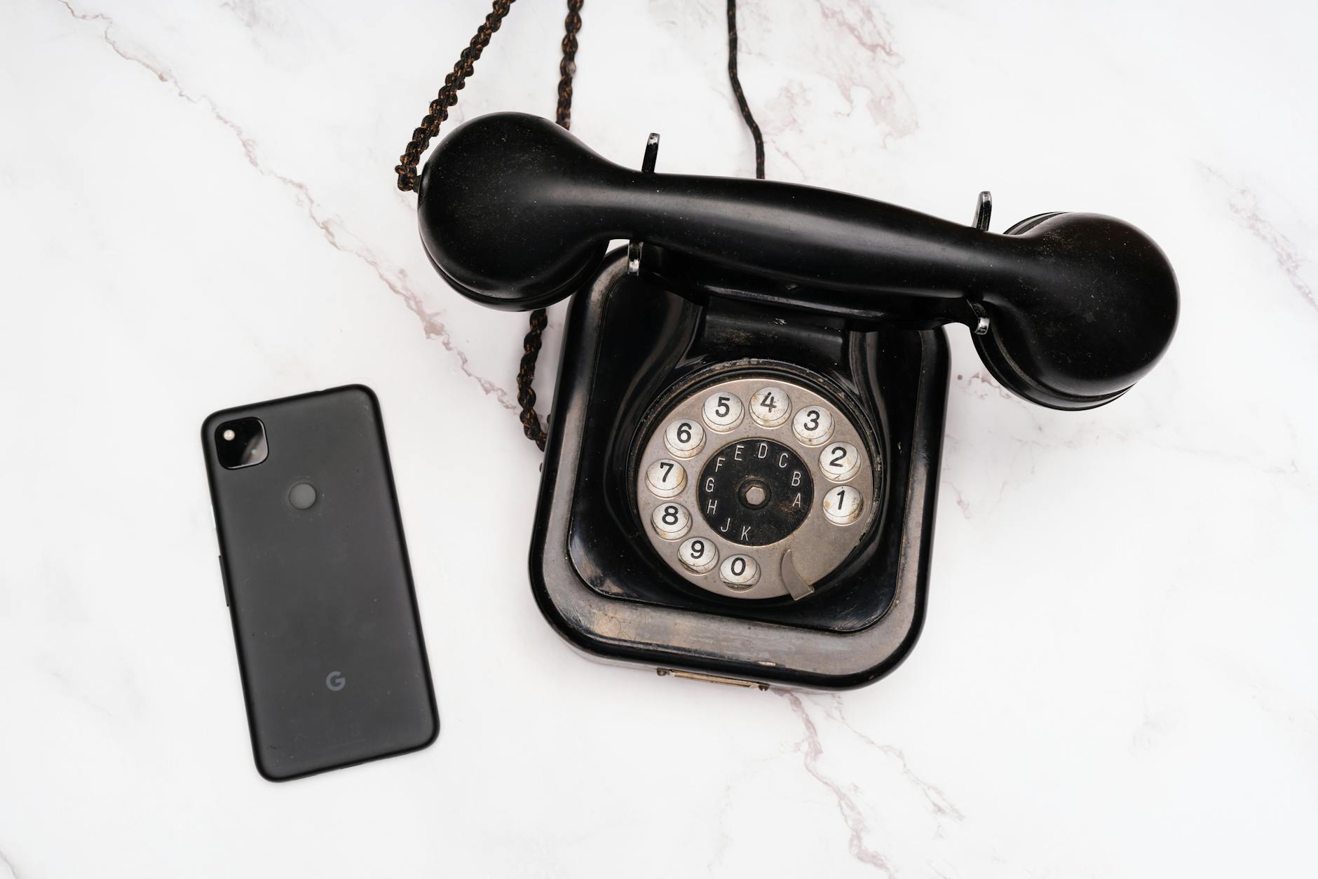 a rotary phone and mobile phone on marble surface