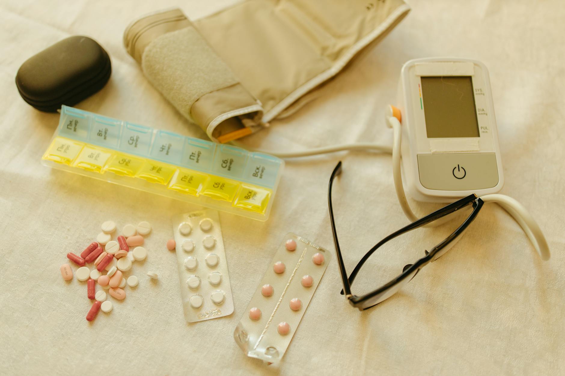 medicines and digital blood pressure monitor on white fabric